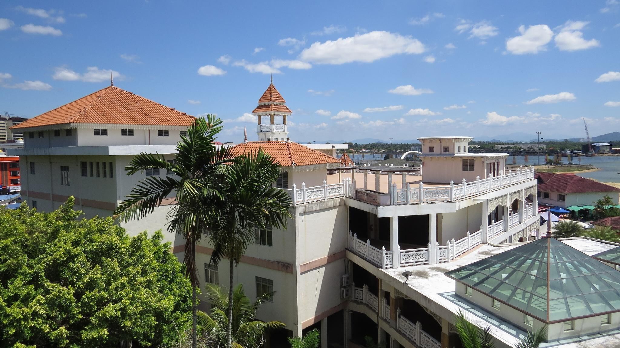 A multi-story building with a red-tiled roof, a bell tower, and a view of a body of water.