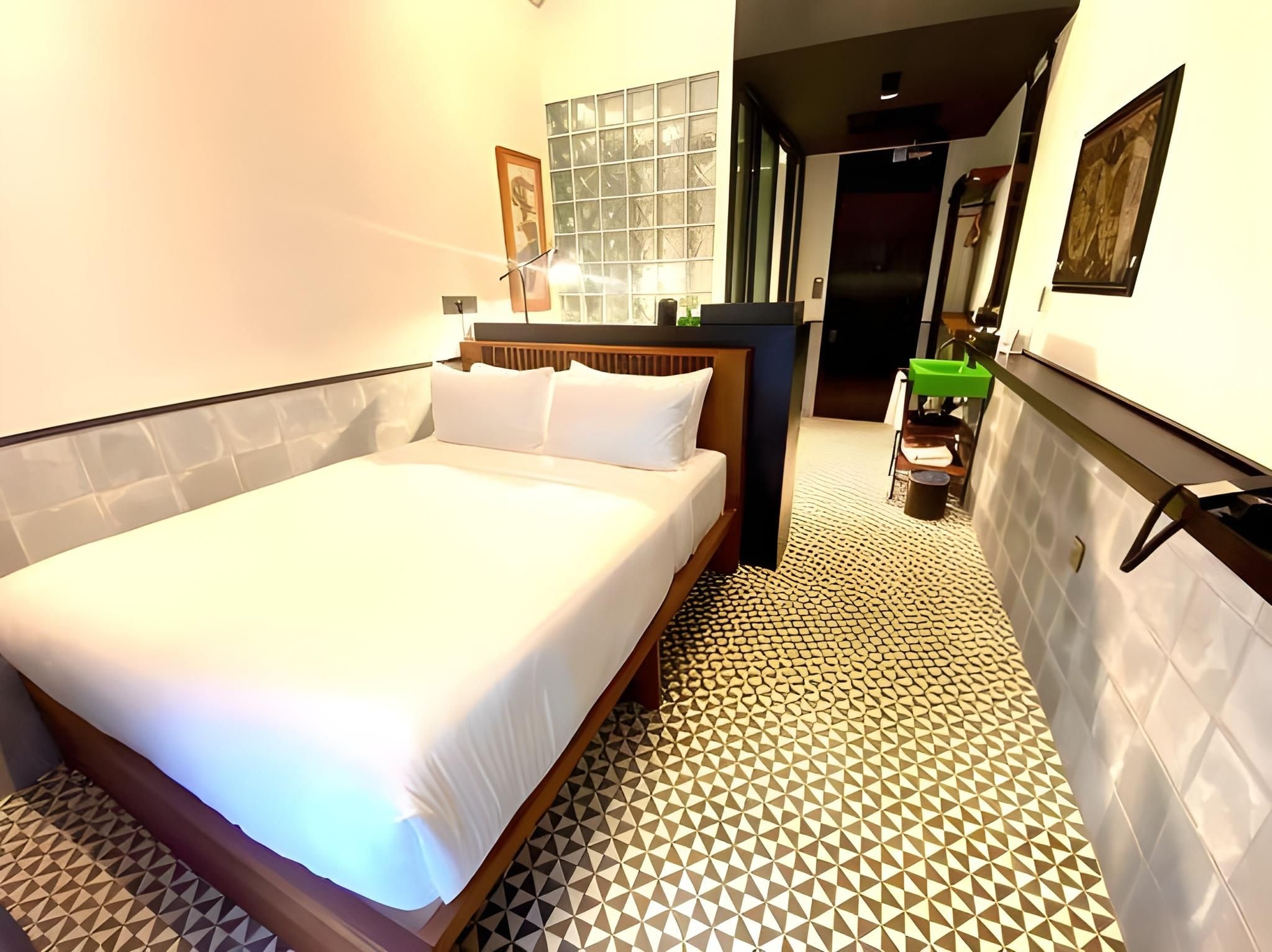 A hotel room with a bed, a small bedside table, a mirror, and a patterned floor.