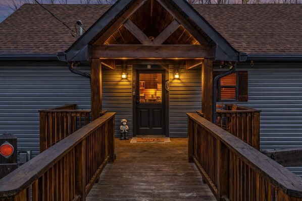 A wooden front porch leading to a dark-colored door with a small statue on the steps. - Freshly Renovated! 3 Pools, Pickleball, Hot Tub, Game Rm! (Gatlinburg)