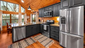 A modern kitchen with dark cabinets, stainless steel appliances, and a wooden ceiling. - Freshly Renovated! Pickleball, Hot Tub, Game Rm! (Gatlinburg)
