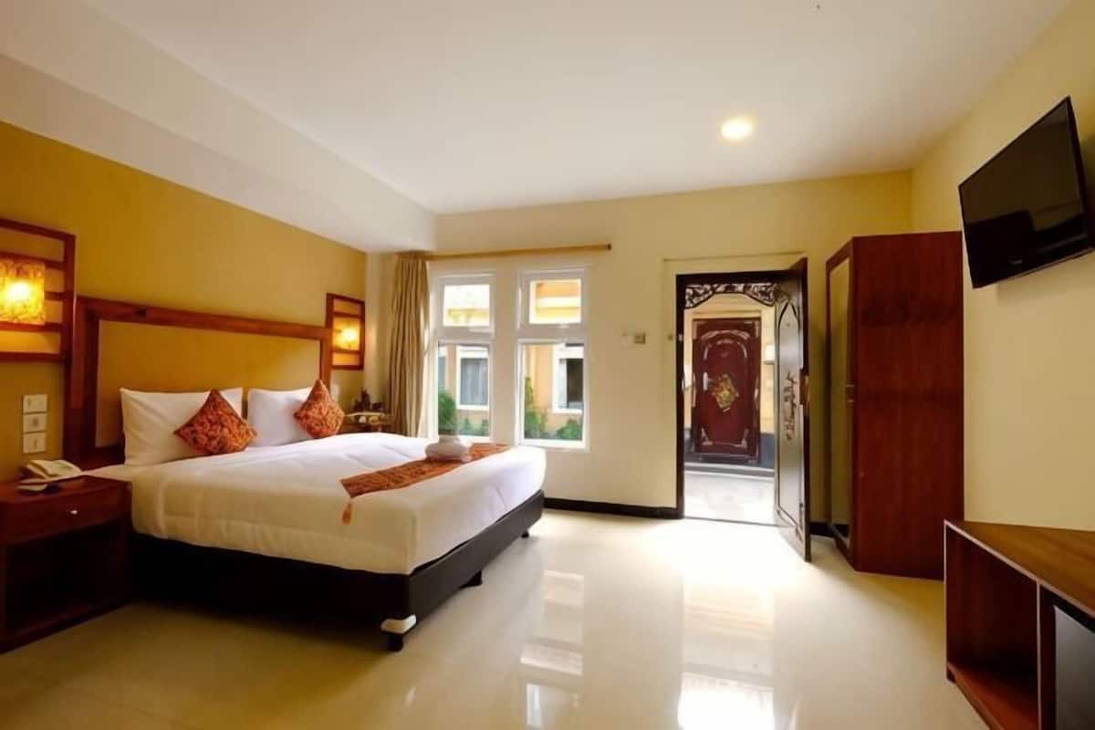 Une chambre d’hôtel équipée d’un lit, d’une télévision, d’une armoire en bois et d’une porte donnant sur un balcon.