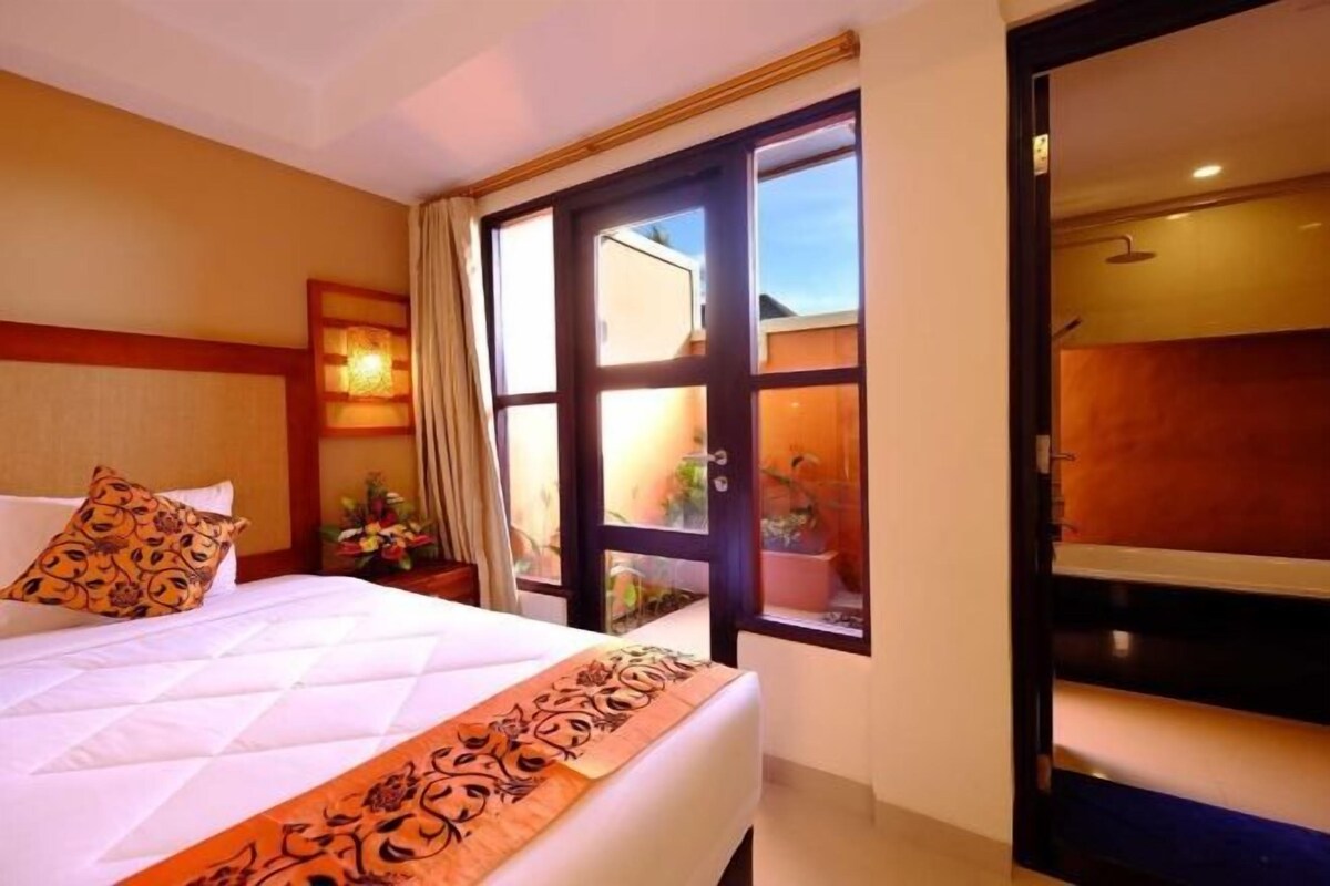 A hotel room with a bed, a nightstand, a window with curtains, and a view of the outside.