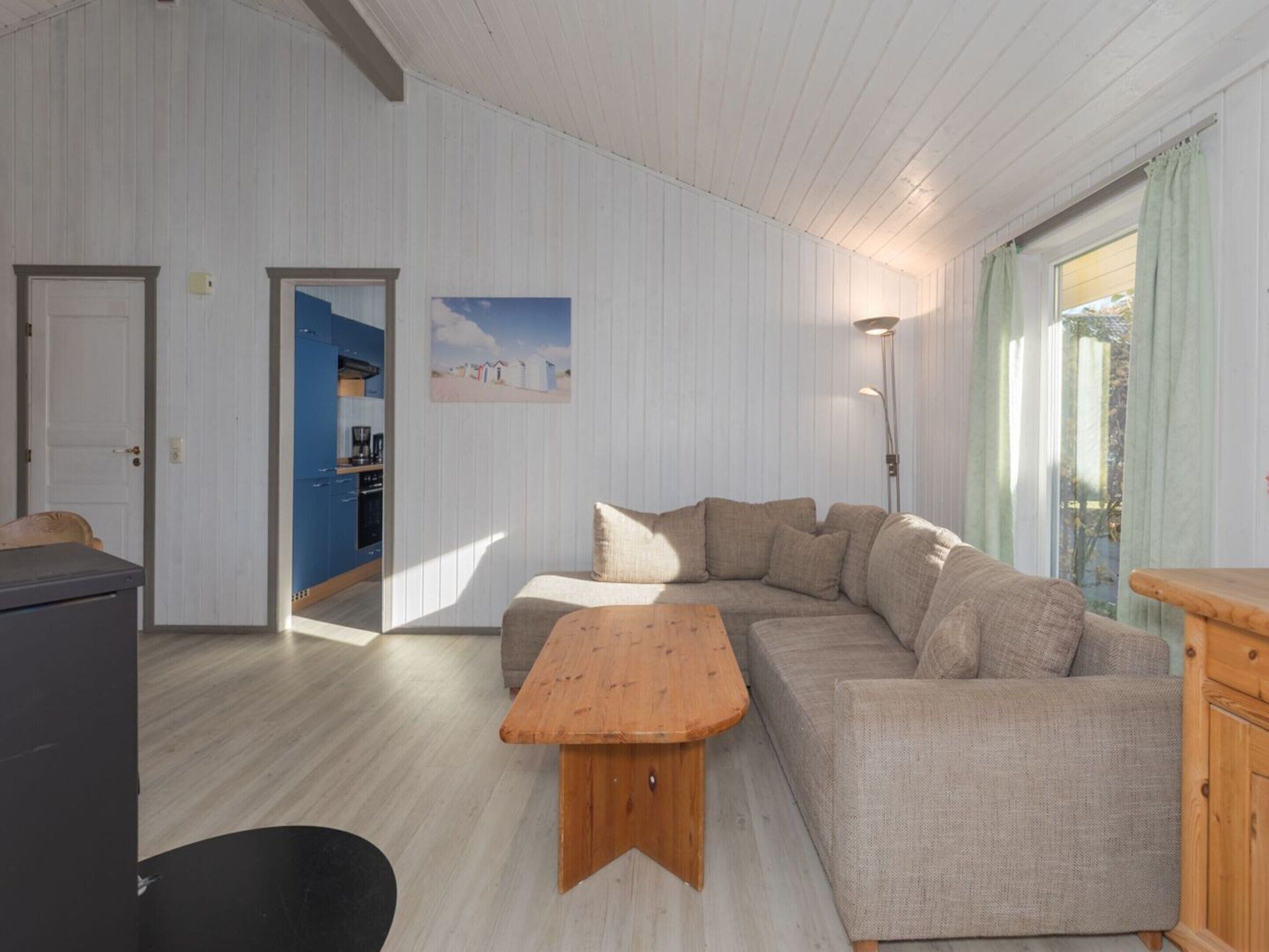 A living room with a sectional sofa, a wooden coffee table, and a kitchen visible through an open door.