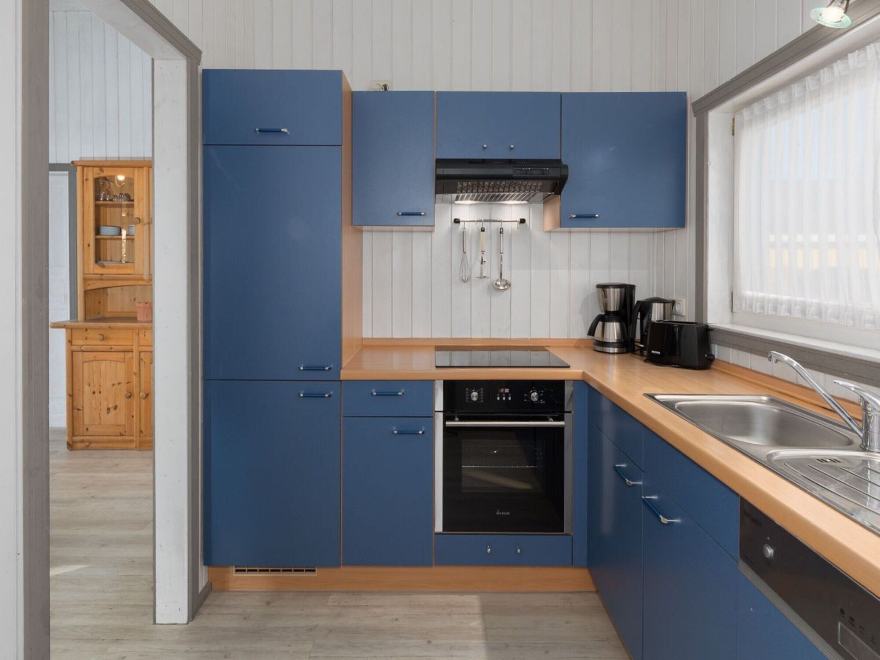 A modern kitchen with blue cabinets, a built-in oven, and a coffee maker.