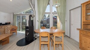 A spacious room with a large dining table, wooden chairs, a built-in wood stove, and a view through large windows. - Ferienhaus mit Sauna im Ferienpark Mirow (Mirow)