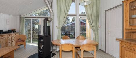 A spacious room with a large dining table, wooden chairs, a built-in wood stove, and a view through large windows.