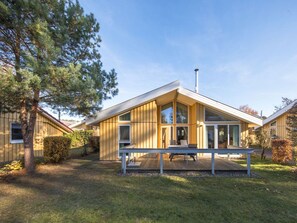 Une maison moderne, de plain-pied, dotée de grandes fenêtres et d’une façade en bois.