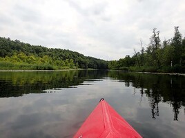 A calm river with a red canoe in the foreground.