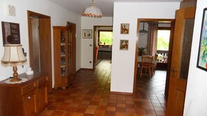 Un pasillo amplio con suelo de baldosas, mobiliario de madera y una zona de comedor con mesa y sillas.
