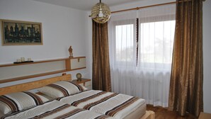 Un dormitorio con una cama doble, una mesita de noche, una lámpara, un cuadro en la pared y una ventana con cortinas.