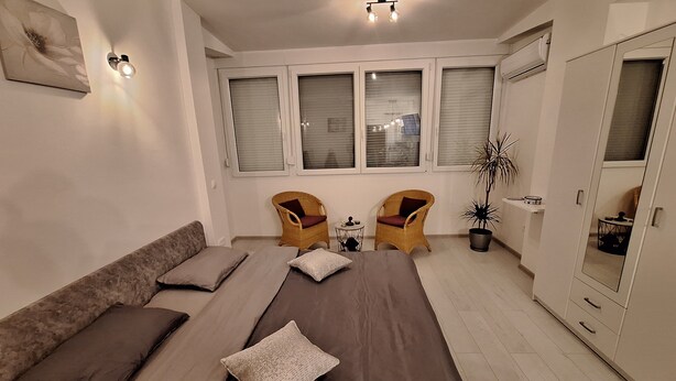A modern bedroom with a large bed, two wicker chairs, a small table, and a potted plant. - Mystic Grey Studio Apartment (Ploce)