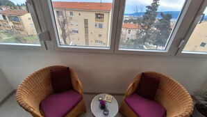 A balcony with wicker chairs and a small table, overlooking a residential area with buildings and a distant view of the sea. - Mystic Grey Studio Apartment (Ploce)