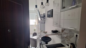 A modern kitchen with white cabinets, a microwave, a kettle, and hanging pendant lights. - Mystic Grey Studio Apartment (Ploce)