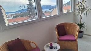 A room with two wicker chairs with purple cushions, a small round table with a vase and candles, and a potted plant. - Mystic Grey Studio Apartment (Ploce)