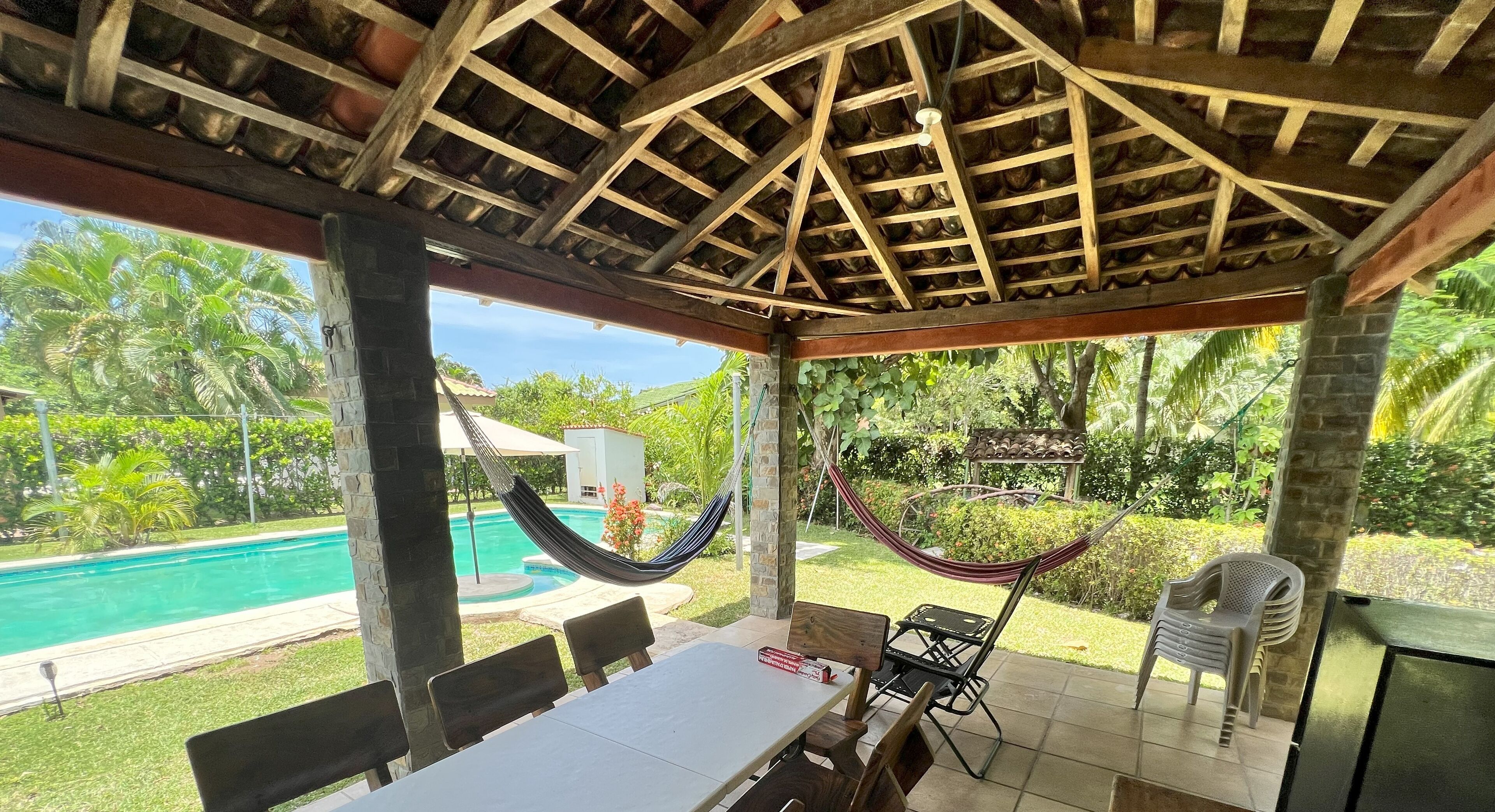 Ein überdachter Außenbereich mit Pool, einer Hängematte und einem Tisch mit Stühlen.