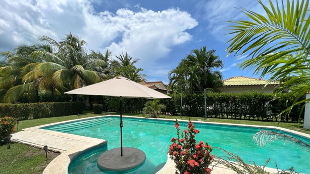 A swimming pool with a beige umbrella, surrounded by palm trees and a well-maintained lawn.