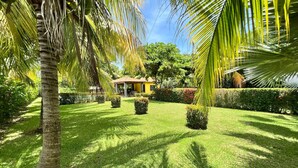 A well-maintained garden with a gazebo, palm trees, and neatly trimmed hedges.