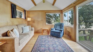 A cozy room with a wooden ceiling, a large window, a sofa, a chair, and a patterned rug. - Private Dock & Lake Views: Home on Lime Lake (Machias)