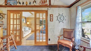 A cozy room with a wooden floor, a large window with a view, a wooden chair, and a door leading to another room. - Private Dock & Lake Views: Home on Lime Lake (Machias)