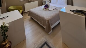 A hotel room with a bed, bedside table, a desk, a chair, a radiator, a window with curtains, and a ceiling light. - İnebolu EsKonak Otel (Inebolu)