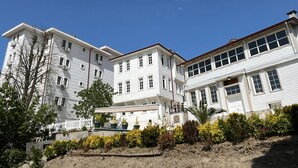 A multi-story building with a white facade, multiple windows, and a small garden area with various plants. - İnebolu EsKonak Otel (Inebolu)