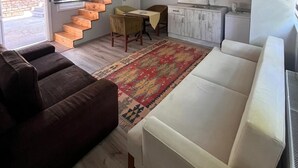 A modern living room with a sofa, a coffee table, and a patterned rug. There is a staircase leading to an upper level, and a kitchen area with cabinets and a sink. - İnebolu EsKonak Otel (Inebolu)