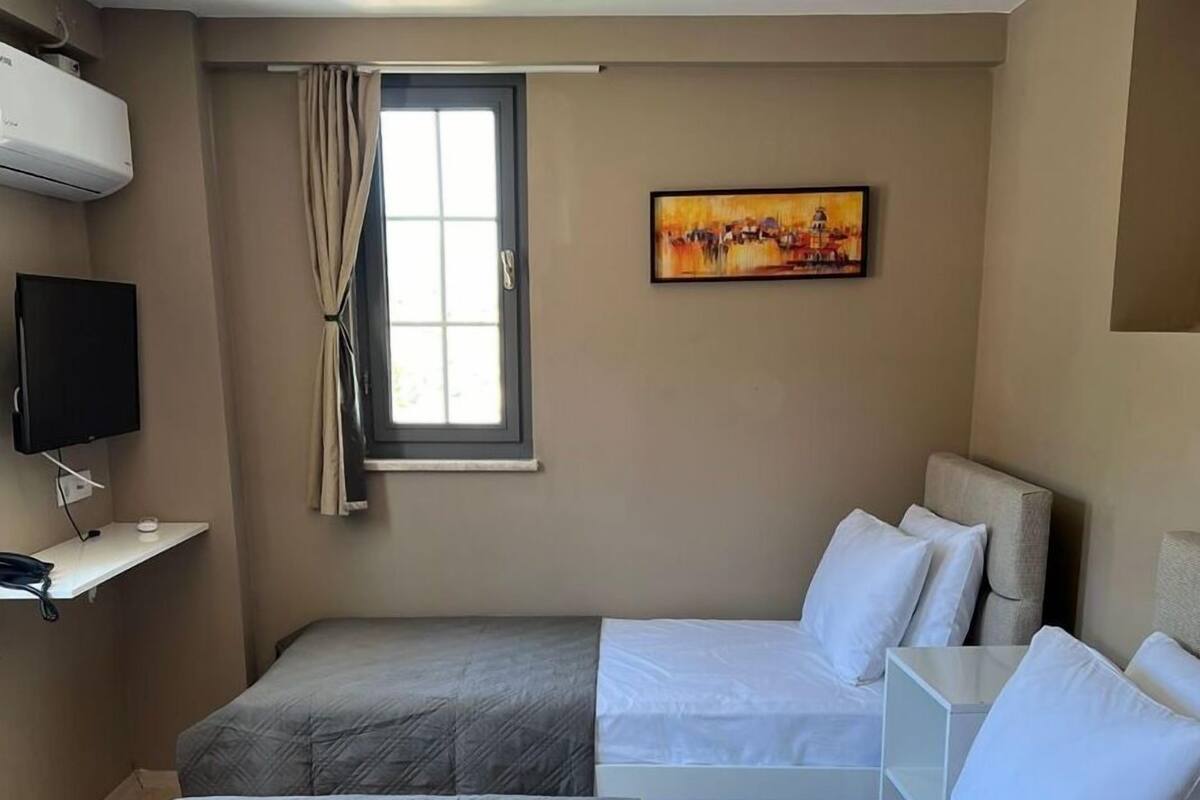 Ein Hotelzimmer mit zwei Betten, einem Fernseher, einem Gemälde und einem fenster mit Vorhängen.