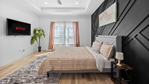 Une chambre à coucher moderne, avec un lit, un téléviseur fixé au mur, un ventilateur de plafond et une fenêtre avec des rideaux.