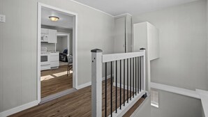 A modern interior with a staircase, wooden flooring, and a kitchen area visible through an open doorway.