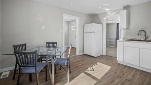 A modern kitchen with a glass dining table, wooden chairs, white cabinets, and a built-in sink.