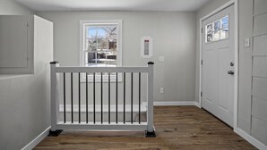 A hallway with a wooden floor, a white railing, and a door with a window.