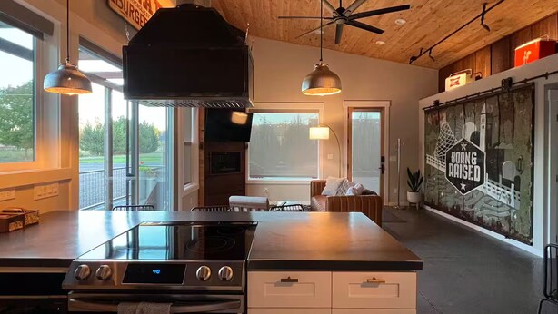 Een moderne keuken met een centraal eiland, roestvrijstalen apparatuur, hangende lampen en uitzicht op de omgeving.