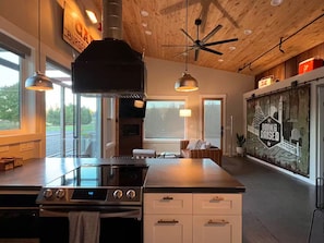 A modern kitchen with a central island, stainless steel appliances, pendant lighting, and a view of the outdoors. - The Shop on Cherry--private hot tub! 8 minutes to downtown in semi-rural area (Spokane)