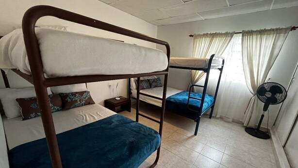 A dormitory room with bunk beds, a standing fan, and a window with curtains. - Casa Naranjo (Caicedonia)