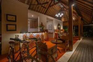 A wooden deck with a thatched roof, a dining area with chairs and a table, and bicycles parked against the wall.