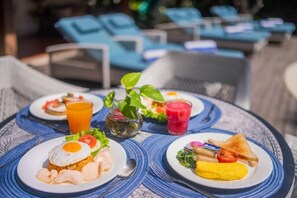 A table with plates of food and drinks, surrounded by lounge chairs. - Kama Village Sanur (Bali)