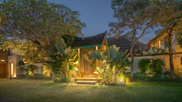 A traditional building with a tiled roof and a small porch, surrounded by lush greenery and a paved courtyard.