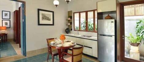 A kitchen with a dining table, chairs, a refrigerator, and a window with a view of greenery.