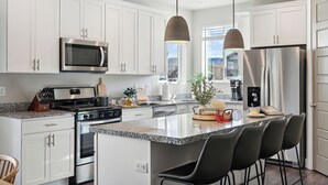 A modern kitchen with white cabinetry, stainless steel appliances, a granite countertop, and a central island with bar stools. - 2 Suites|Hot tub|Arcade|BBQ|ESPN|H20+|No Cheap TP (Midway)