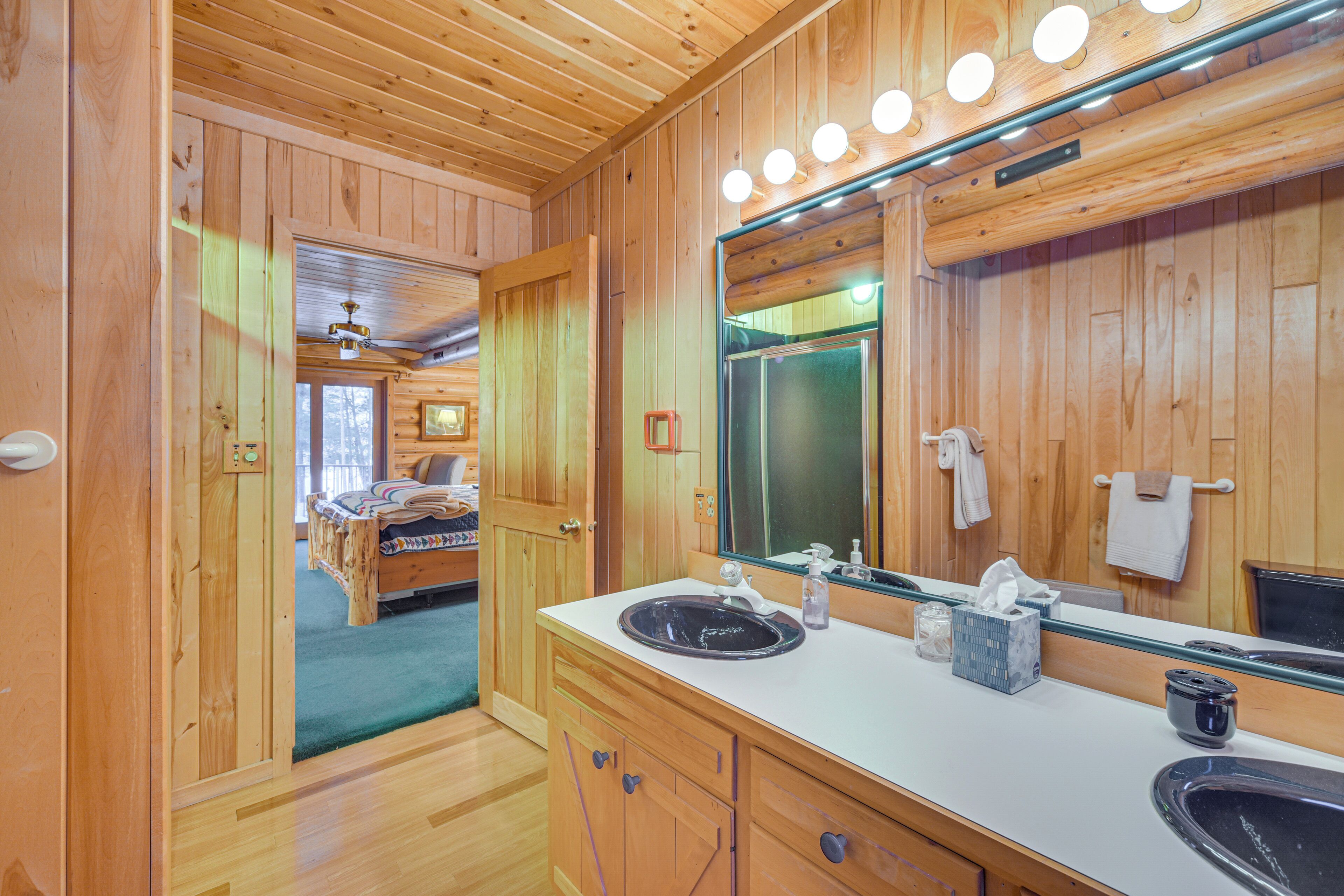 L’intérieur d’un chalet en bois comprend une salle de bain dotée d’un grand miroir, de deux lavabos et d’un meuble-lavabo en bois.