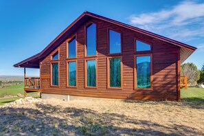 A wooden cabin with multiple large windows, a deck, and a clear view of the surrounding landscape.