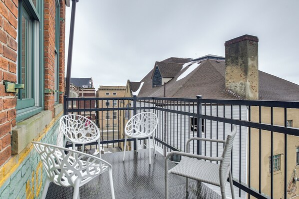 Un balcon doté de balustrades en métal et de deux chaises en osier blanches.