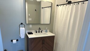 A bathroom with a white sink, dark wooden cabinet, white tiled floor, and a shower curtain.