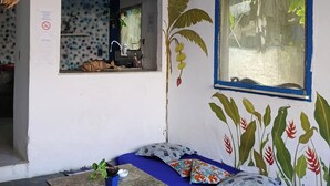 Een kamer met een blauwe bank, een kleine tafel, een raam met uitzicht en een plantenmuurschildering.