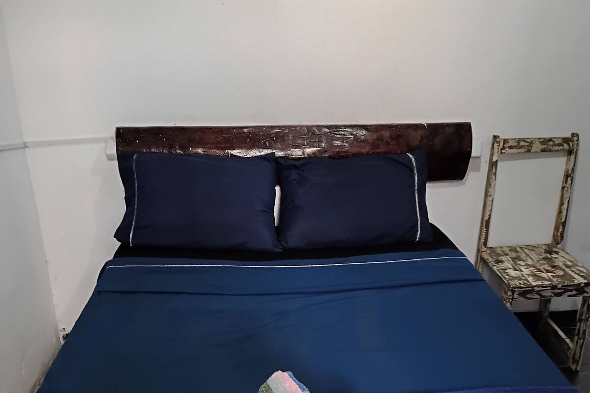 Ein Bett mit dunkelblauer Bettdecke und Kissen, ein gestreiftes Handtuch und ein rustikaler Holzsessel.