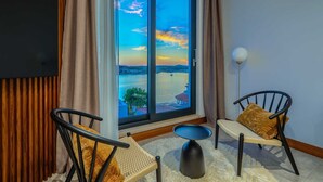 A modern living room with a large sliding glass door leading to a scenic view of a river and sunset. There are two black chairs with woven seats and a small round table. - Luxurious 5-BR Villa for 10 with Panoramic Views and Heated Pool (Zatoglav)