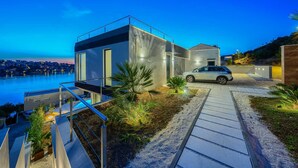 A modern house with a car parked in front, a balcony, and a view of the water. - Luxurious 5-BR Villa for 10 with Panoramic Views and Heated Pool (Zatoglav)