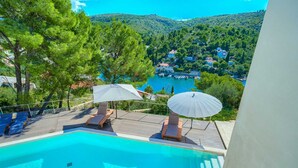 A swimming pool with lounge chairs and umbrellas, overlooking a coastal village and hills. - Spacious 4-Bedroom Villa for 8, with heated pool and sea views (Bobovisca)