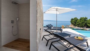 A modern outdoor area with a pool, lounge chairs, and a view of the sea. - Spacious Luxury 5-BR Villa for 10 by the sea, with infinity pool (Omiš)