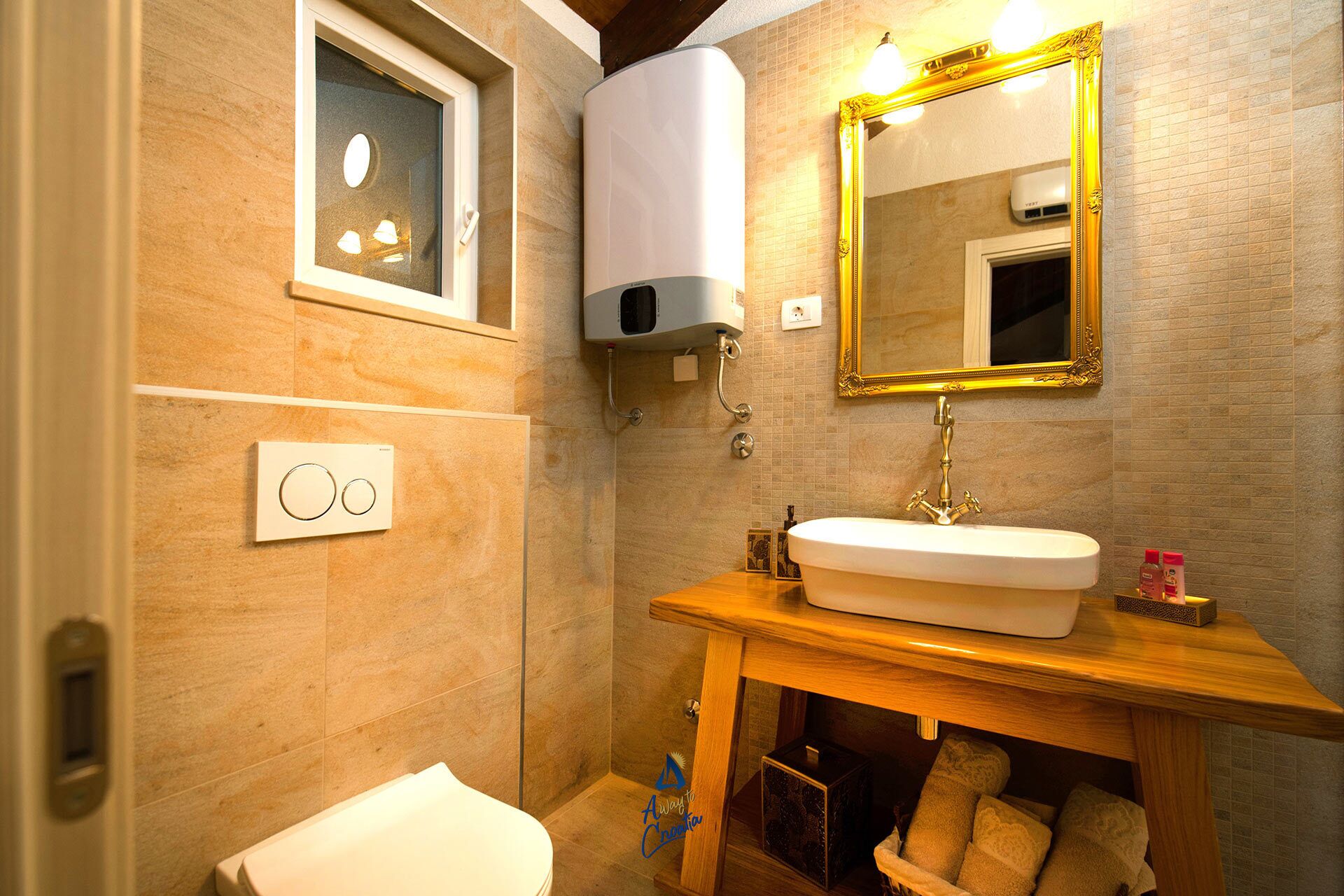 A bathroom with a wooden vanity, a white sink, a gold-framed mirror, and a toilet.